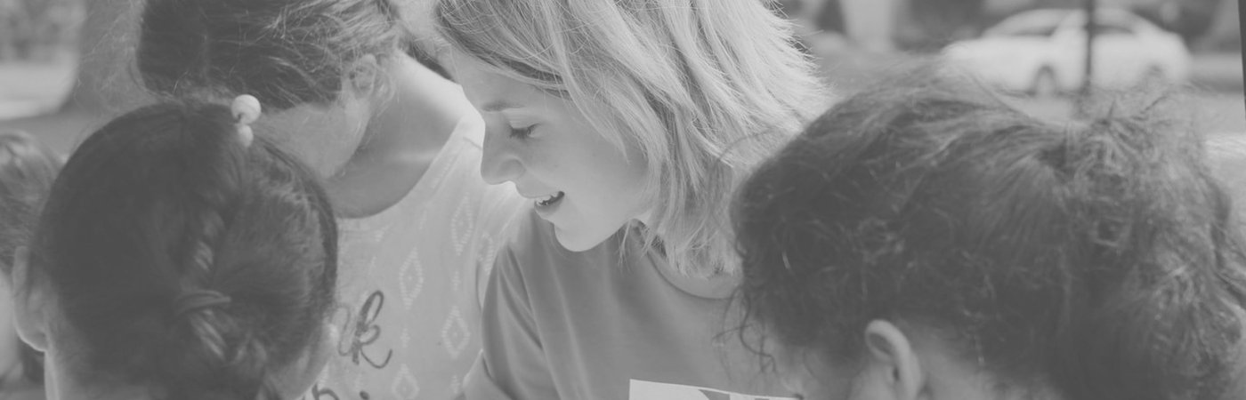 A smiling woman helping a group of children.