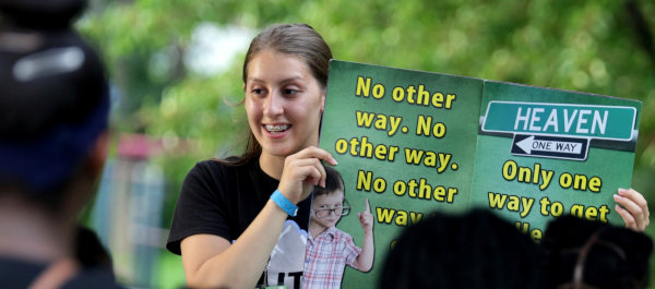 A young woman holding up a lesson book while teaching children.